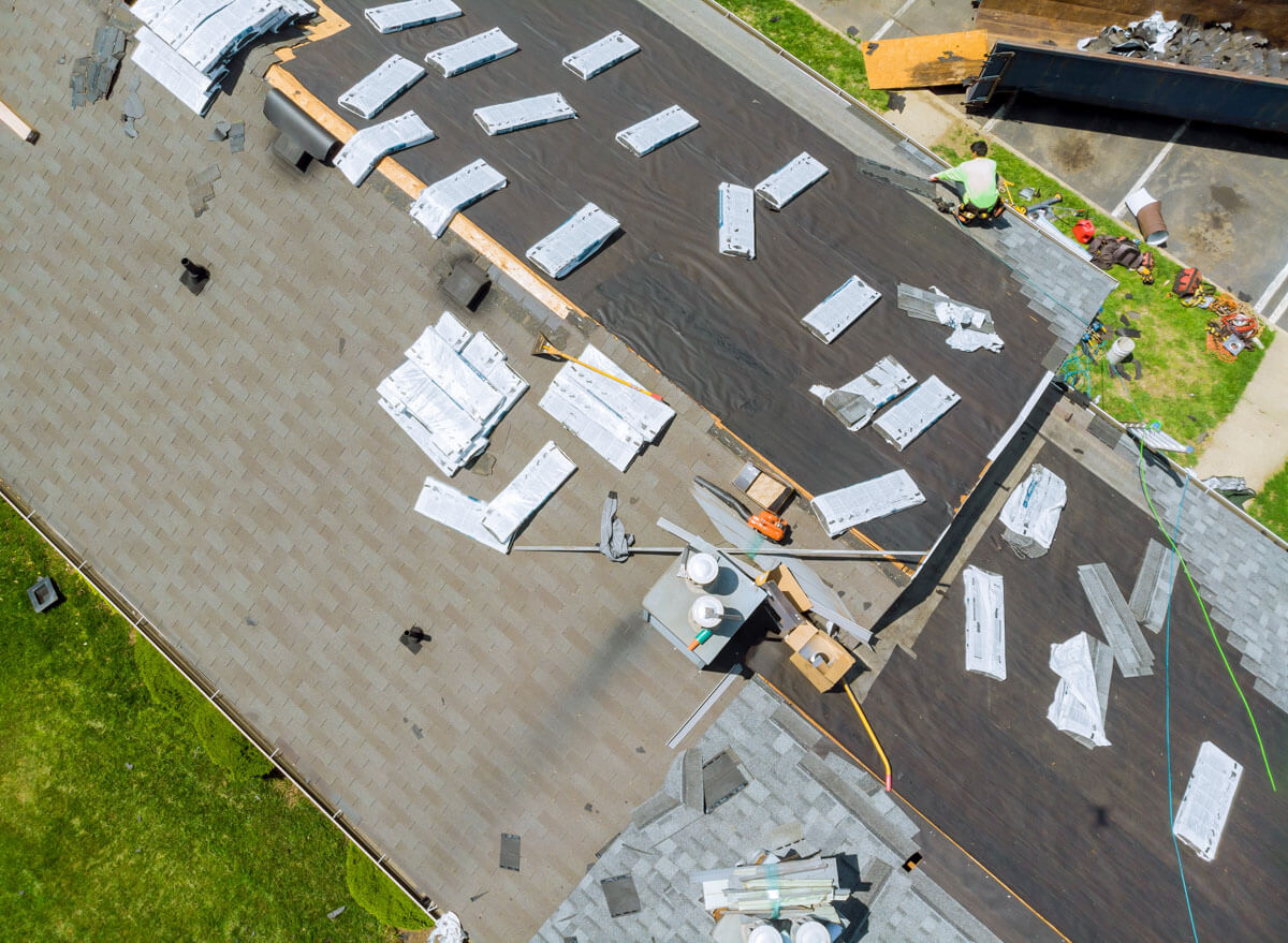 Aerial drone view of an asphalt shingle roof installation in progress with materials scattered on the deck in Mayville and Chautauqua, NY.