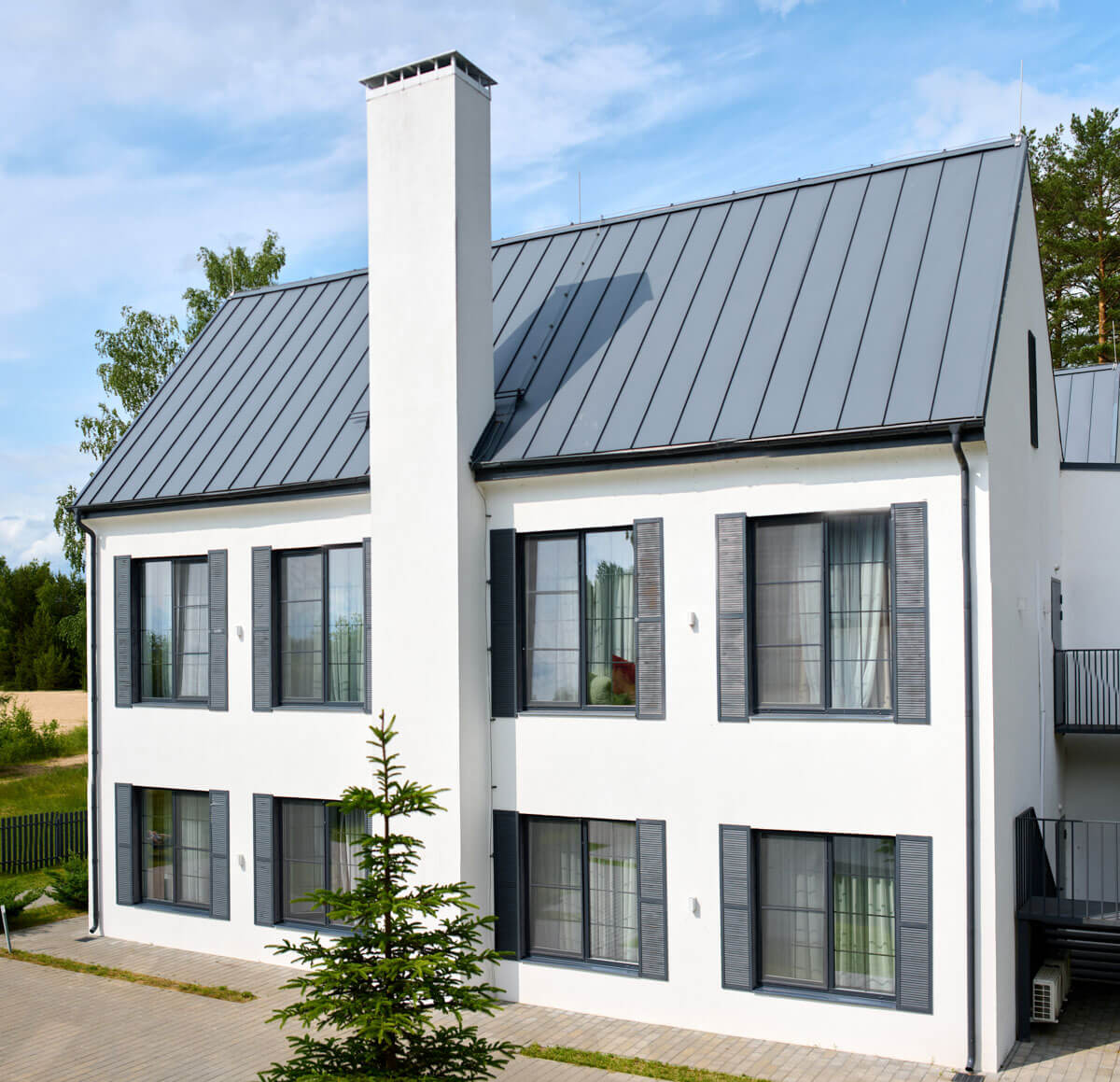 Modern white stucco home featuring dark window shutters and a grey metal roof installed in Meadville, PA.