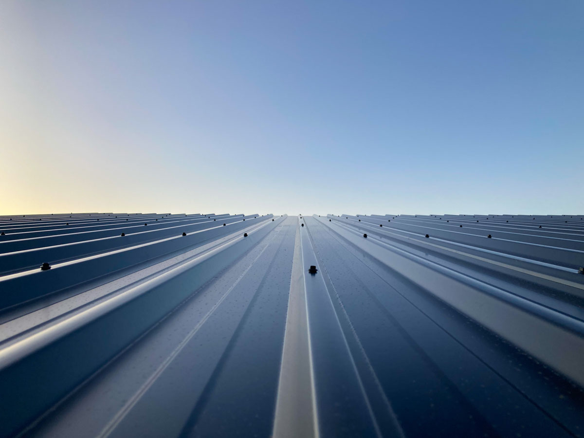 Perspective view of newly installed blue ribbed metal roofing panels stretching toward a clear sky in Westfield, NY.