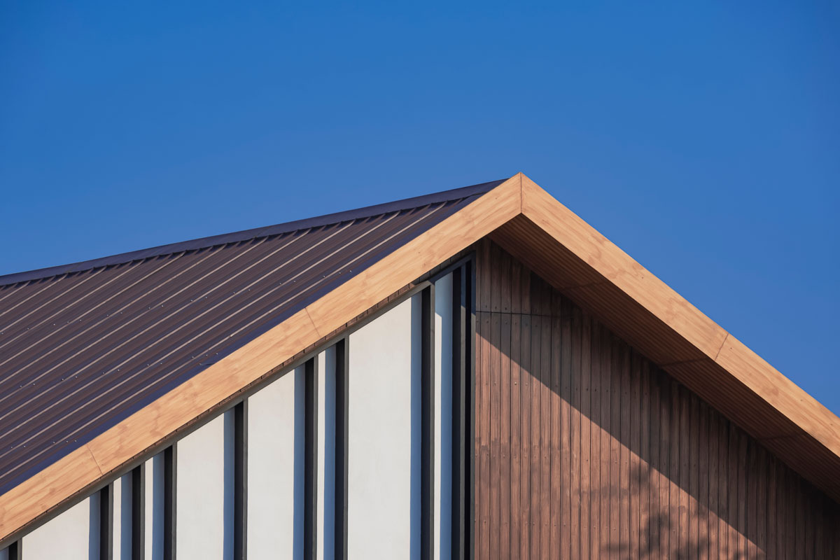 Vertical brown metal siding panels installed on a residential gable home under a blue sky in Westfield, NY.